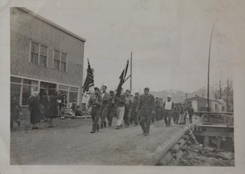 Hoonah Military Marching with Flags in Front of Kanes