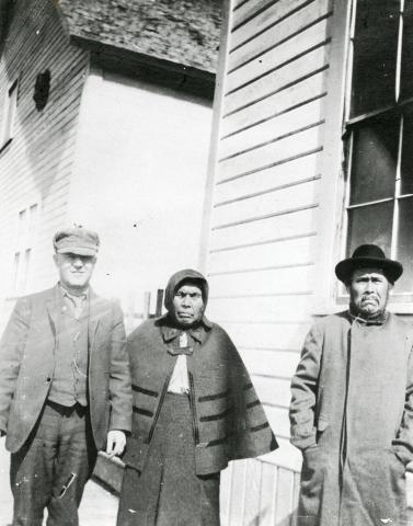 (Hoonah. Two men and a woman standing next to a building.)